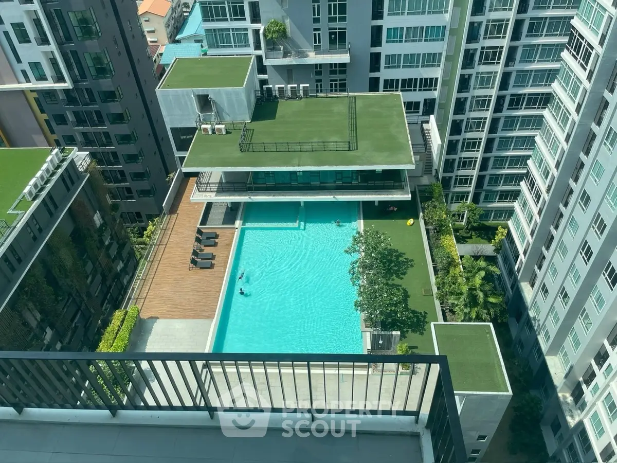 Stunning aerial view of modern condominium with rooftop pool and lush greenery.
