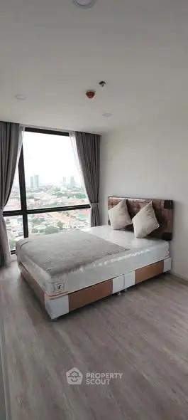 Modern bedroom with large window offering stunning city views, featuring a cozy bed and elegant decor.