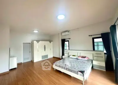 Spacious bedroom with modern furniture and wooden flooring, featuring ample natural light and a minimalist design.