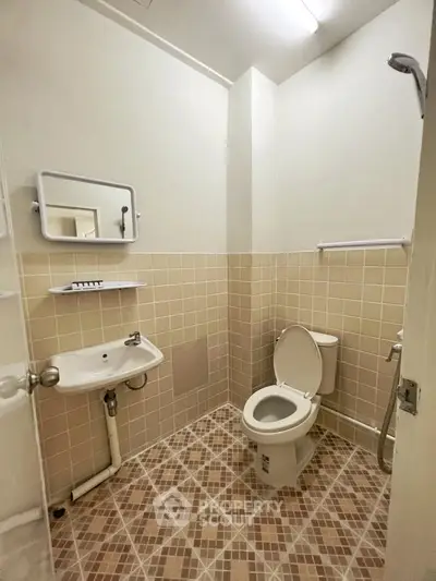 Compact bathroom with tiled walls and floor, featuring a toilet, sink, and mirror.