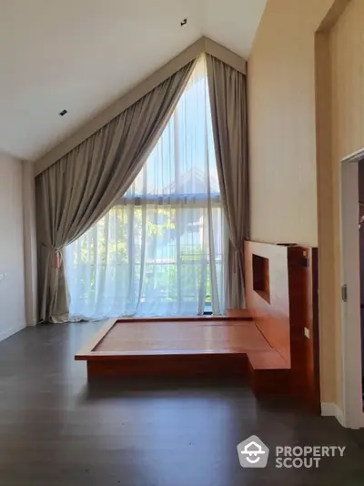 Spacious bedroom with large window and elegant curtains, featuring a unique wooden platform bed.