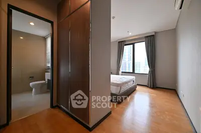 Modern bedroom with ensuite bathroom and city view, featuring wooden flooring and large windows.