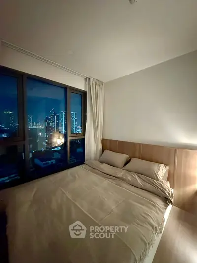 Cozy bedroom with city skyline view, featuring a comfortable bed and large windows for natural light.