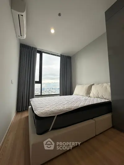Modern bedroom with city view, featuring a comfortable bed and large window.