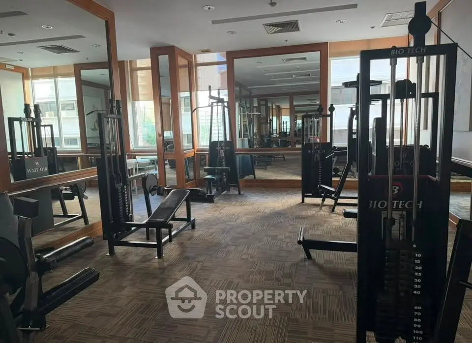 Spacious gym with modern fitness equipment and large mirrors in a residential building.
