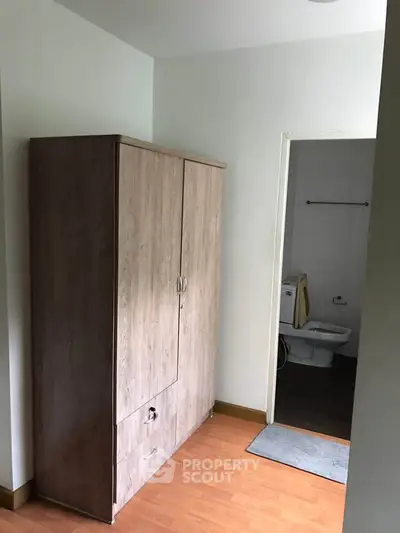 Compact room with wooden wardrobe and adjacent bathroom, ideal for efficient living.