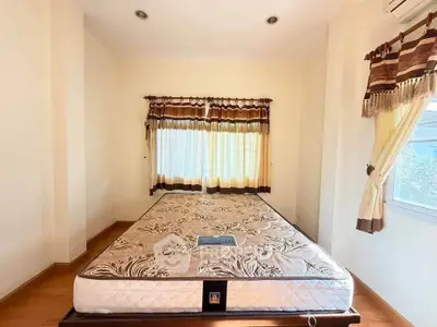 Bright bedroom with large windows and elegant curtains, featuring a comfortable mattress on a wooden floor.