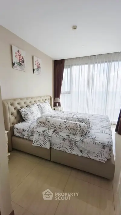 Elegant bedroom with plush bed and floral decor, featuring large windows for natural light.