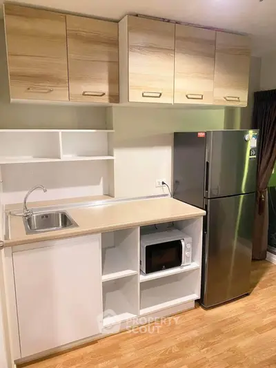 Modern kitchen with sleek cabinets, stainless steel fridge, and built-in microwave in a cozy apartment.