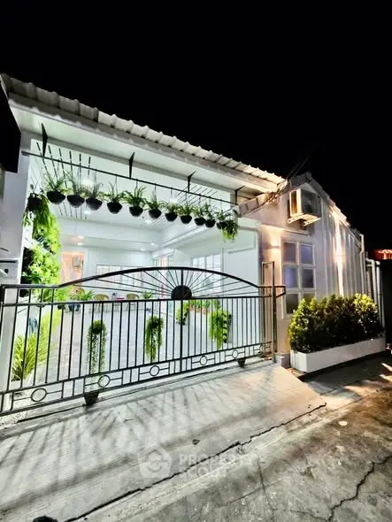 Charming modern house exterior with lush greenery and elegant gate at night.