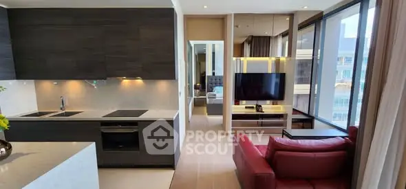 Modern open-plan living room with sleek kitchen and red sofa, featuring large windows and stylish decor.