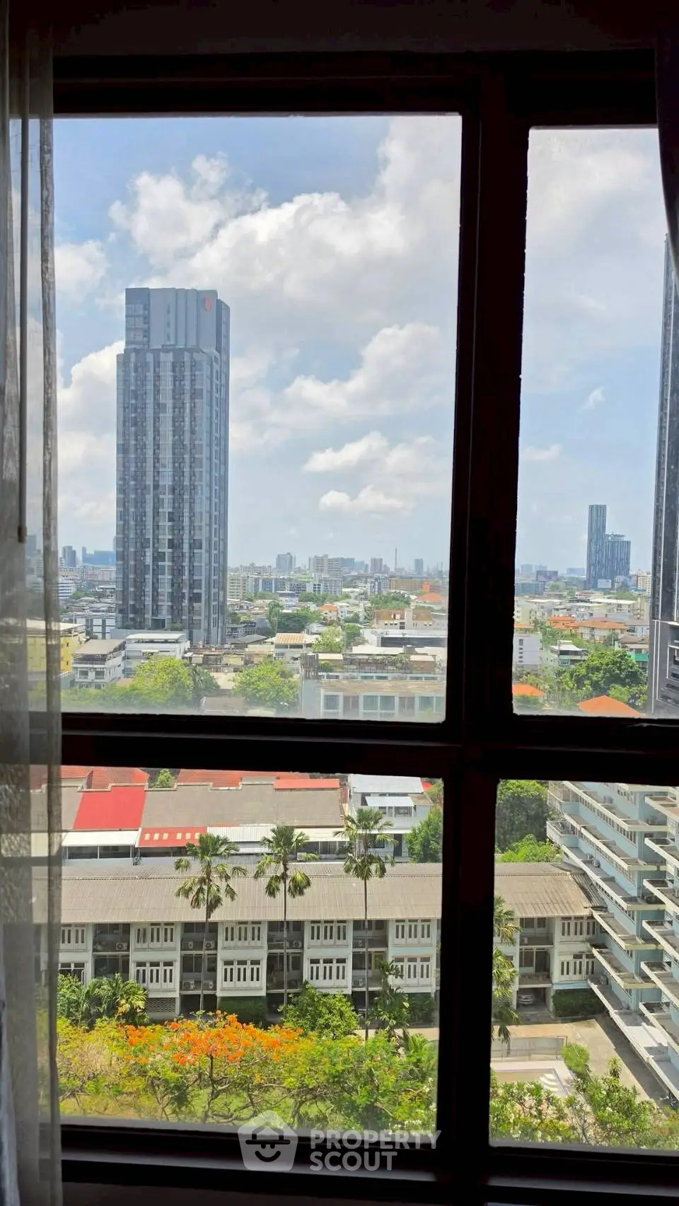 Stunning cityscape view from a high-rise apartment window, showcasing urban skyline and lush greenery.