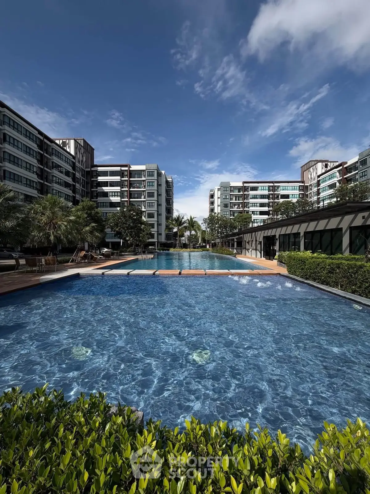 Luxurious apartment complex with stunning pool and lush greenery under a clear blue sky.