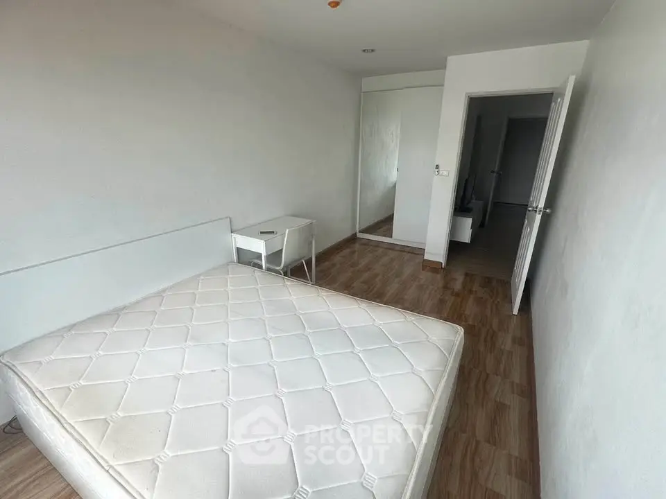 Spacious bedroom with wooden flooring and mirrored closet in modern apartment.
