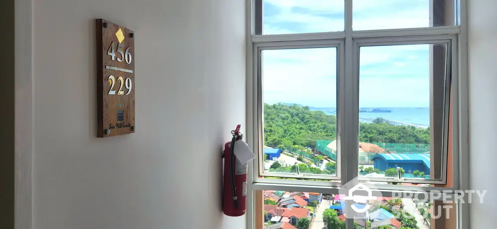 Stunning ocean view from high-rise building window with fire extinguisher and room number sign.