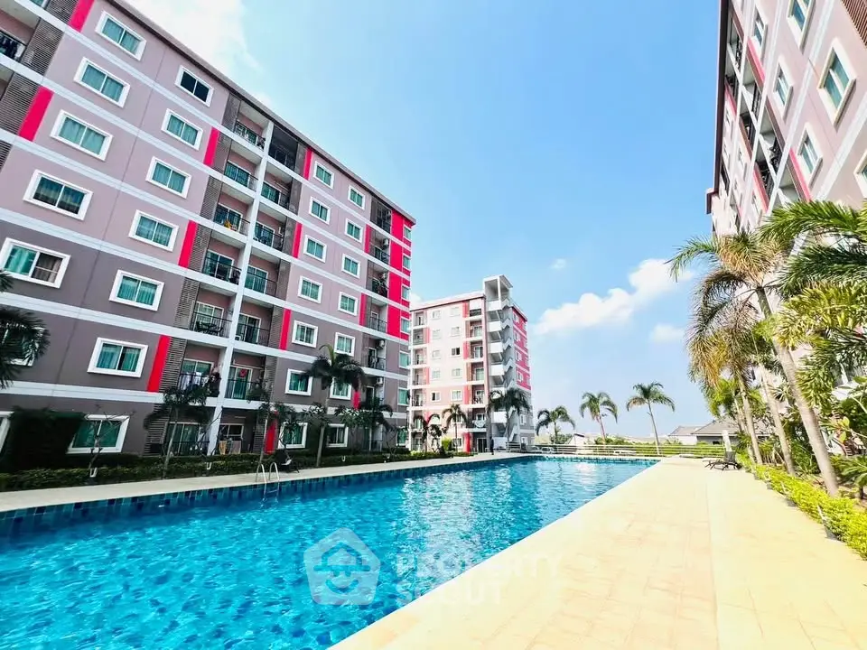 Modern apartment complex with large swimming pool and palm trees under a clear blue sky.