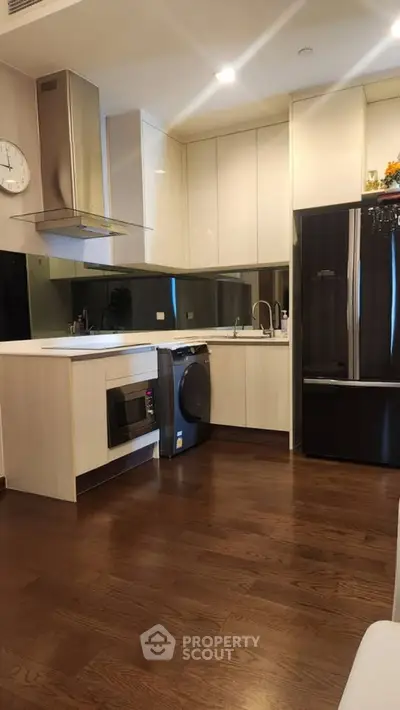 Modern kitchen with sleek appliances and wooden flooring, featuring a washing machine and microwave.