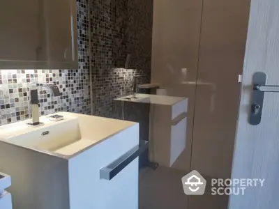 Modern bathroom with sleek design, featuring mosaic tiles, a large mirror, and minimalist white cabinetry for a clean aesthetic.