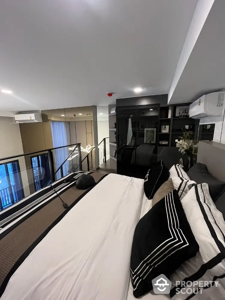 Modern bedroom with stylish decor and glass railing overlooking living space.