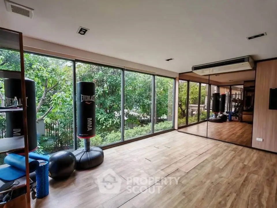 Spacious home gym with floor-to-ceiling windows and lush garden view.