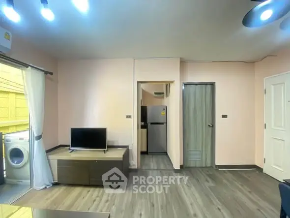 Modern living room with TV, washing machine, and sleek kitchen area in open layout apartment.