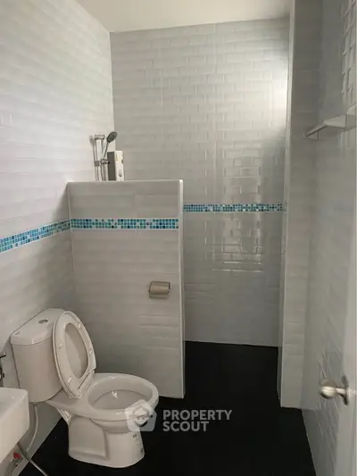 Modern bathroom with sleek white tiles and blue accents, featuring a toilet and shower area.
