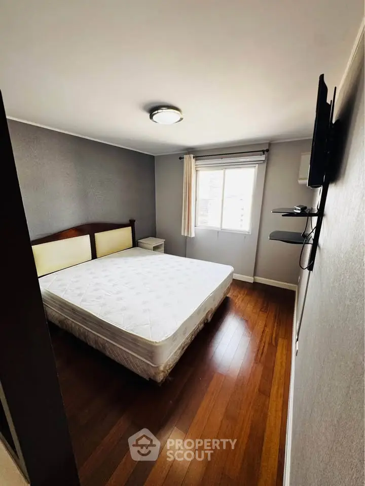 Cozy bedroom with wooden flooring and natural light, featuring a comfortable bed and wall-mounted TV.