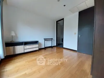 Spacious and well-lit studio apartment with polished hardwood floors, modern kitchenette, and a sleek black entrance door.