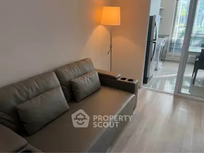 Modern living room with sleek sofa and floor lamp, adjacent to a bright kitchen with washing machine.