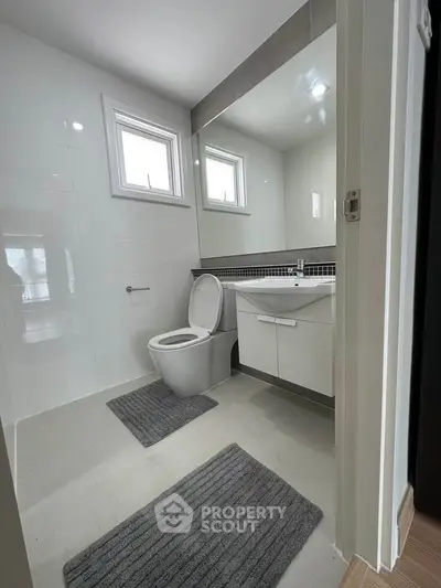 Modern bathroom with sleek design and large mirror, featuring white fixtures and natural light.