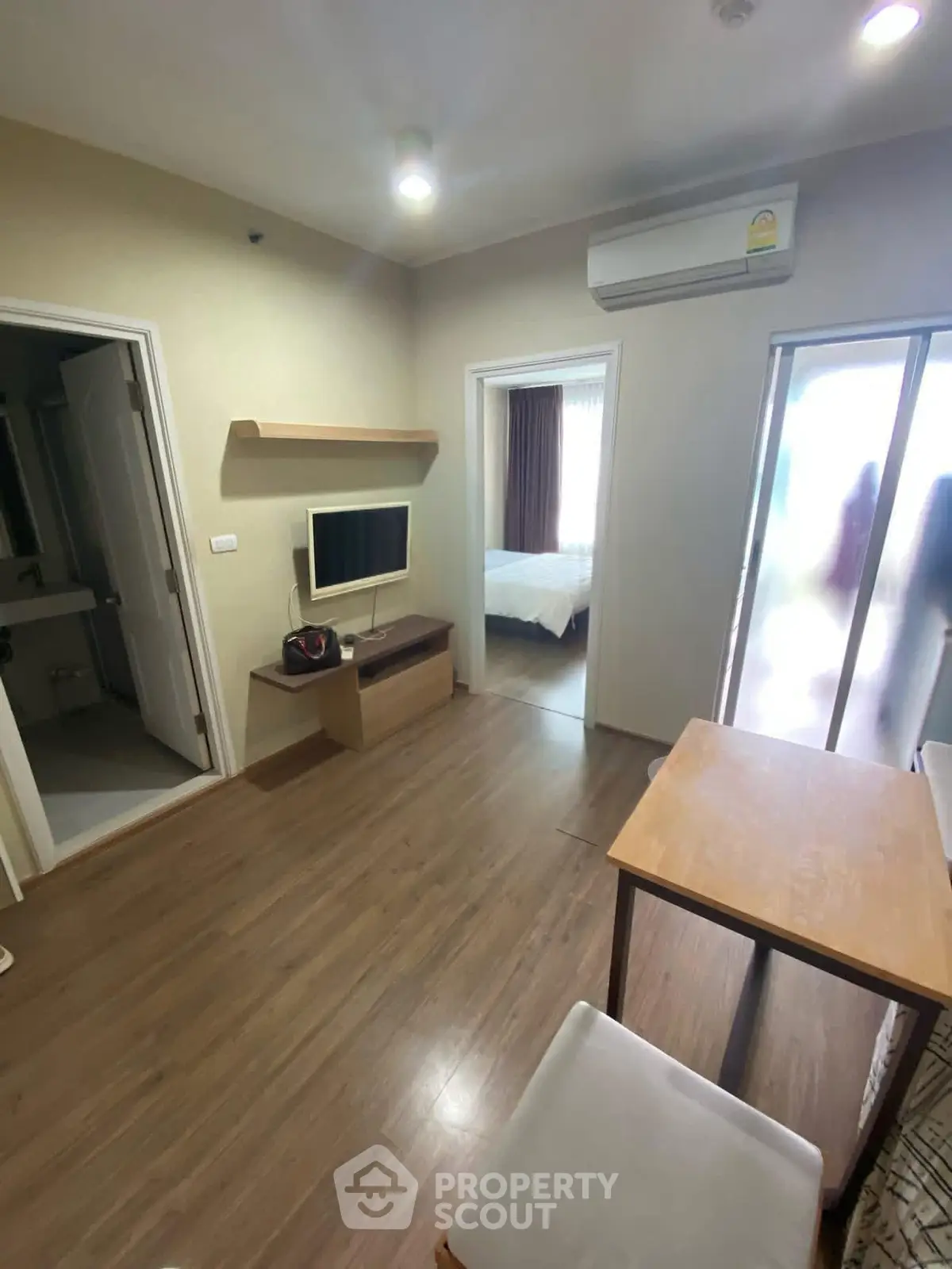 Cozy living room with modern decor and wooden flooring, featuring a wall-mounted TV and air conditioning.