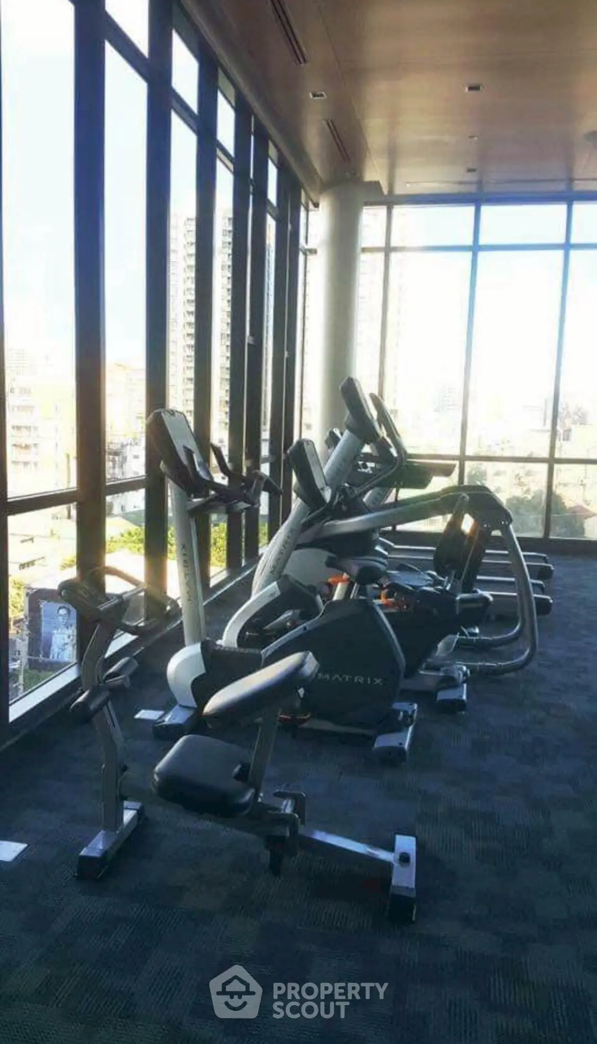 Spacious gym with modern exercise equipment and city view windows.