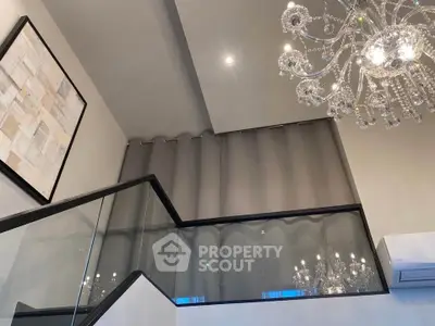 Luxurious modern interior with elegant chandelier and glass railing in a high-ceilinged living space.