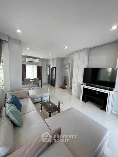 Spacious modern living room with sleek furniture and large TV, perfect for relaxation and entertainment.