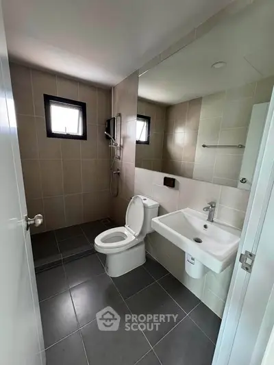 Modern bathroom with sleek fixtures and neutral tiles, featuring a shower and toilet.
