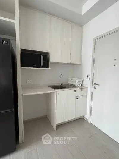 Modern compact kitchen with sleek cabinetry and built-in microwave in a stylish apartment.