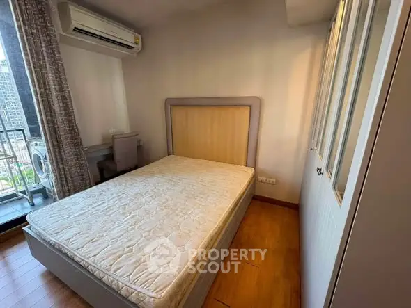 Cozy bedroom with balcony view in modern apartment, featuring air conditioning and wooden flooring.