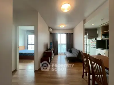 Modern apartment interior with open living room and dining area, featuring wooden flooring and natural light.