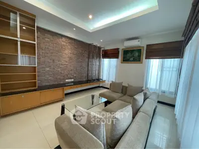 Spacious living room with modern design, featuring a cozy sectional sofa, elegant brick accent wall, and ample natural light.