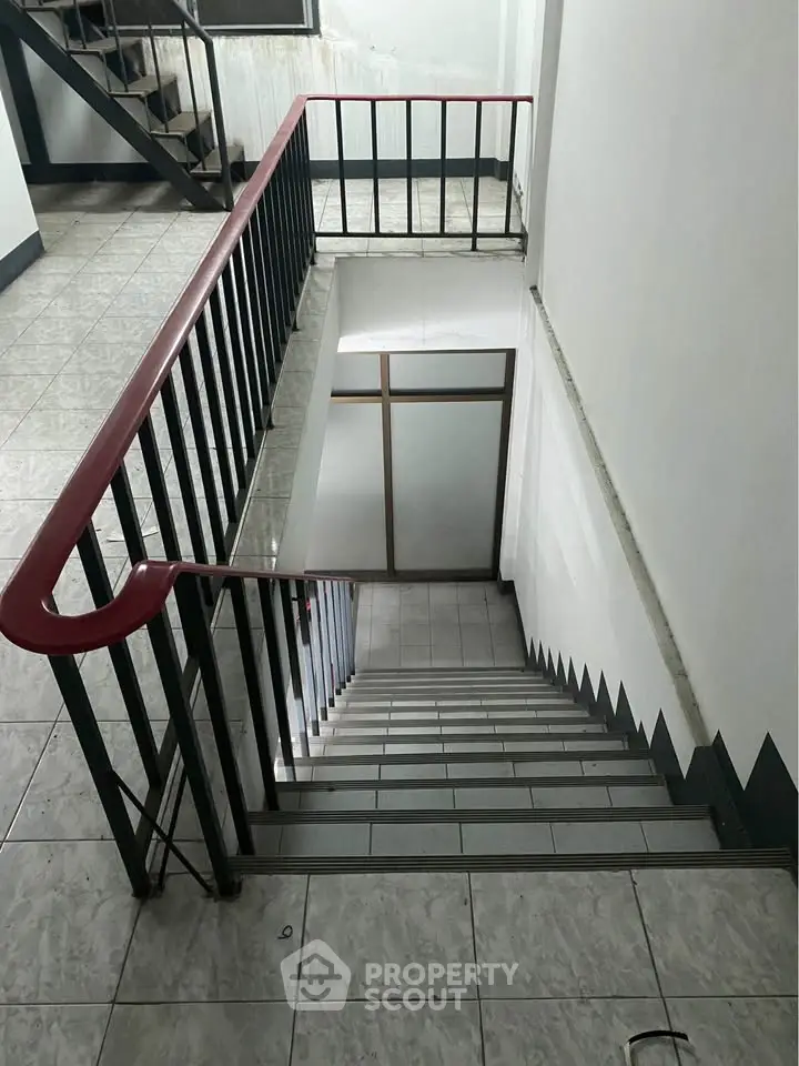 Spacious stairwell in a modern building with sleek metal railings and tiled flooring.