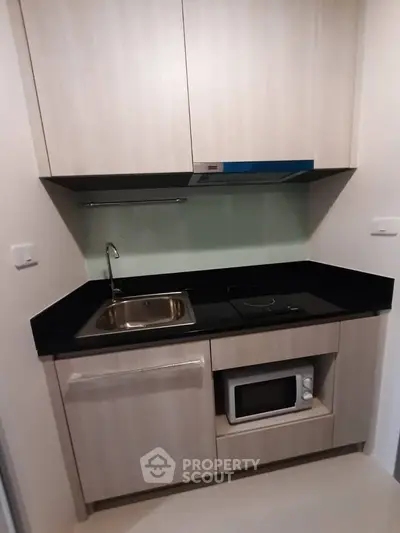 Modern compact kitchen with sleek cabinetry and built-in microwave in a stylish apartment.