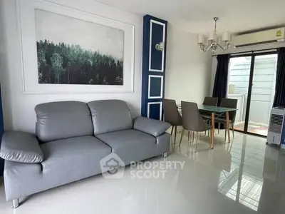 Modern living room with sleek gray sofa and dining area, featuring elegant decor and natural light.
