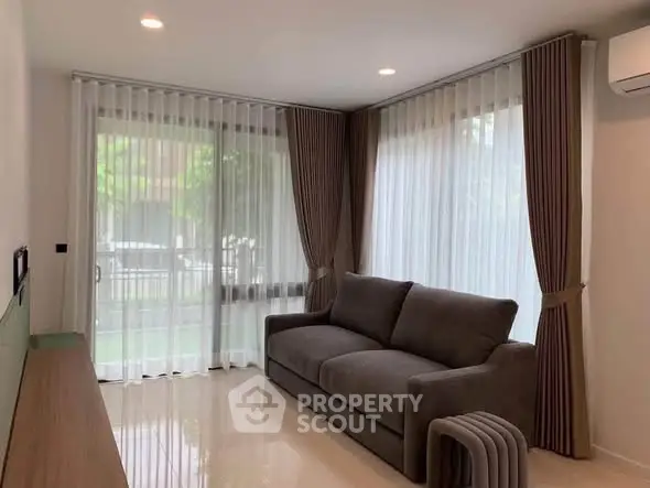 Modern living room with large windows and elegant curtains, featuring a comfortable sofa and sleek flooring.