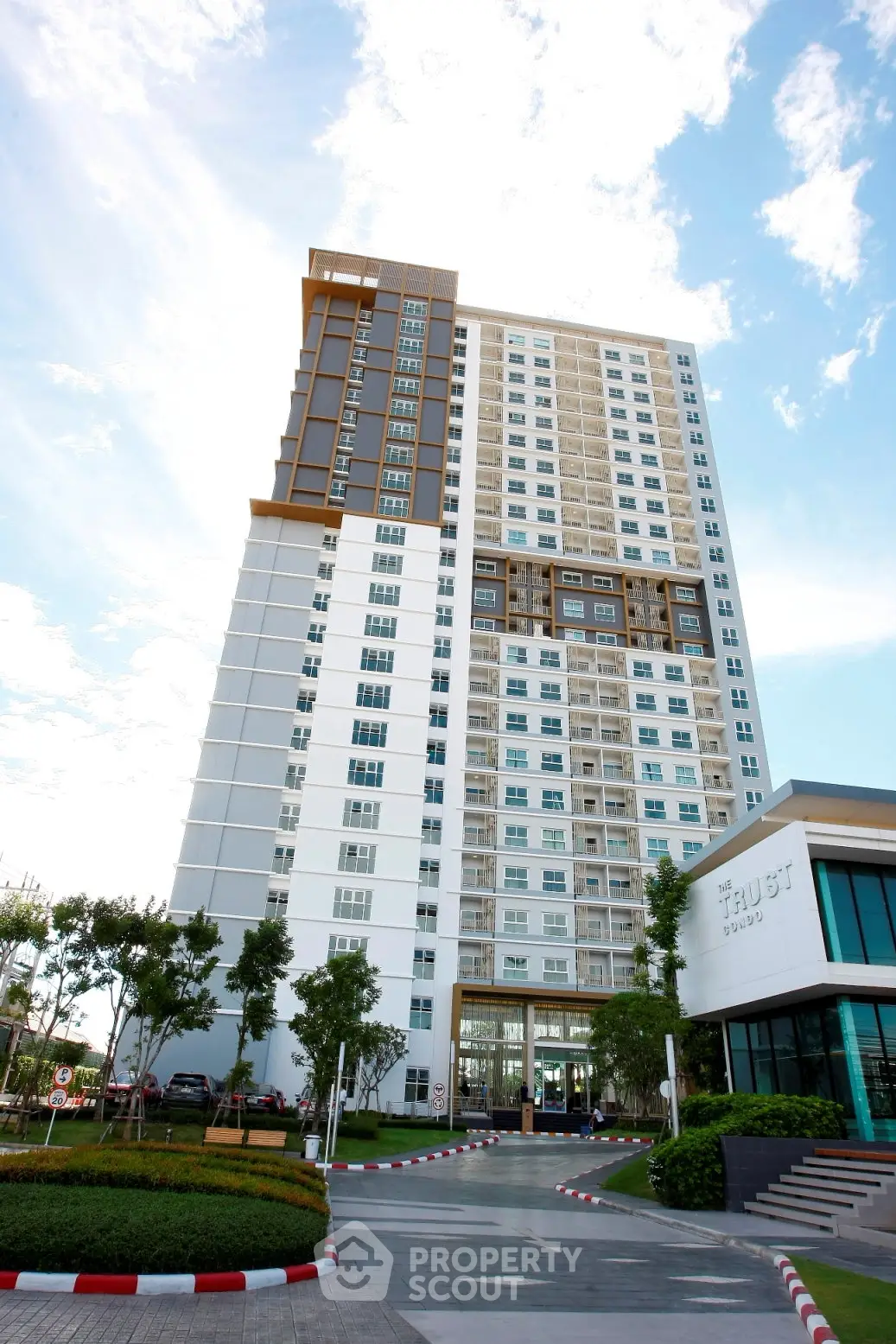 Modern high-rise apartment building with lush landscaping and clear blue sky.