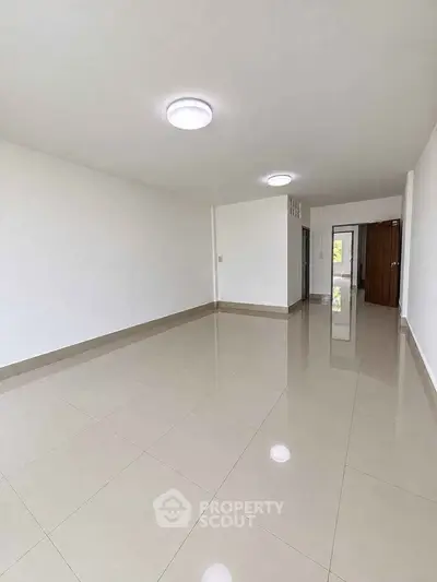Spacious empty living room with glossy tiled floors and modern lighting.