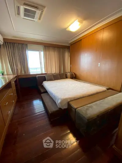 Spacious bedroom with wooden flooring and large window offering natural light.