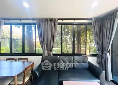 Spacious living room with large windows and garden view, featuring modern furniture and elegant curtains.
