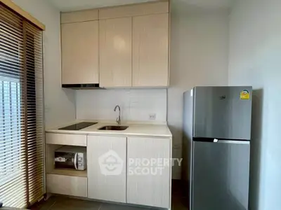 Modern compact kitchen with sleek cabinetry and stainless steel fridge in a cozy apartment.