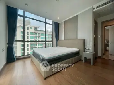 Spacious bedroom with large windows offering a stunning city view, featuring a modern bed and wooden flooring.
