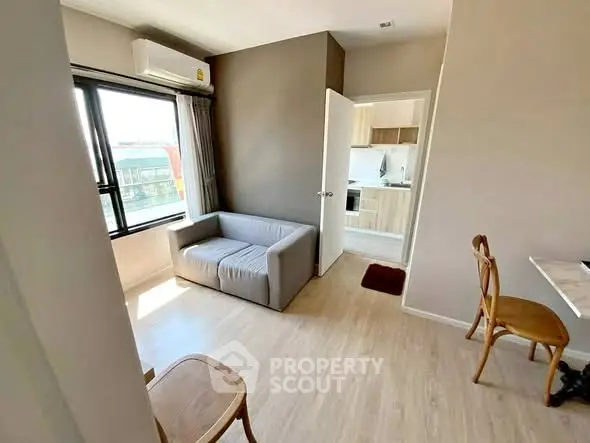 Modern living room with natural light and compact kitchen in open layout apartment.